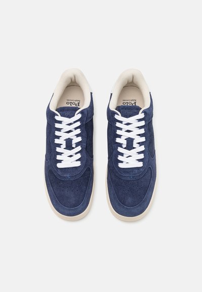 Ναυτικές καστόρινες αθλητικές μπότες με λευκές κορδόνες, αντίθετη κρέμα σόλα από καουτσούκ και τρυπητό μπροστινό μέρος; διαθέτουν λογότυπο στη γλώσσα.