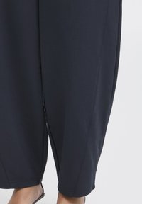 Pantalon ample bleu marine foncé en tissu doux avec jambe effilée, fentes latérales et finition lisse et unie.