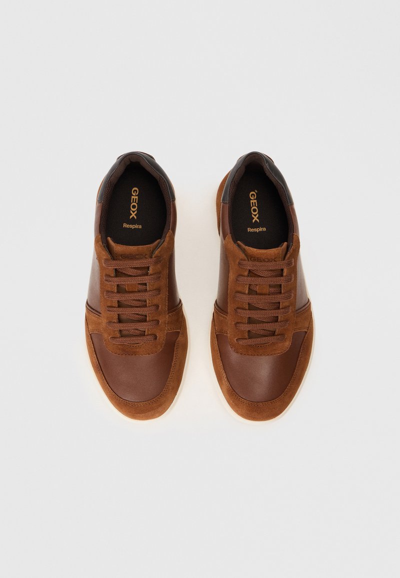 Baskets brunes en cuir et suède avec une surface supérieure lisse, des lacets plats et une semelle en caoutchouc blanche. Présente une marque Geox à l'intérieur.