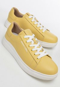 Sneaker in pelle gialla con finitura testurizzata, lacci bianchi e dettaglio logo discreto. Suola in gomma bianca elevata per il massimo comfort.