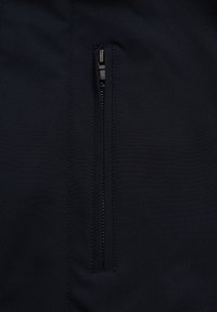 Musta kangas, jossa on sileä pinta ja pystysuora vetoketjullinen tasku. Ommel on hienovarainen ja integroitu suunnitteluun.