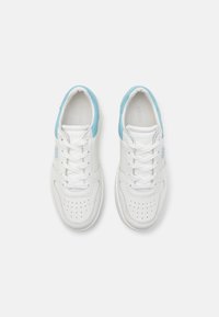 Un paio di sneakers bianche e azzurro chiaro di Guess con lacci, punte perforate e marchio sulle linguette e sui lati, viste dall'alto.
