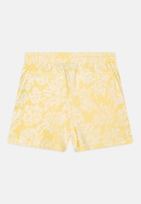 Shorts jaunes avec un motif floral blanc, dotés d'une taille élastique et de deux poches arrière. Le tissu a une texture douce et lisse.