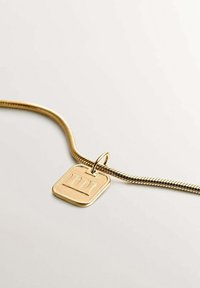 Collar de cadena de serpiente dorada con colgante cuadrado grabado con el número romano tres, fotografiado sobre una superficie blanca.