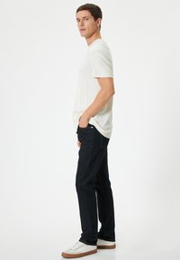 Camiseta de manga corta gris claro combinada con jeans azules oscuros. Los jeans presentan costuras naranjas y un ajuste relajado. Calzado: zapatillas blancas.