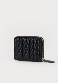 Μαύρο κομψό δερμάτινο πορτοφόλι με επένδυση και ασημένιο φερμουάρ και ταμπελάκι, το οποίο απεικονίζεται σε απλή φωτεινή επιφάνεια και ελαφρώς γωνιακή γωνία.