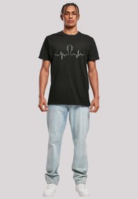 Black cotton t-shirt featuring a white heartbeat line graphic with a guitar silhouette, short sleeves, and a classic crew neckline.