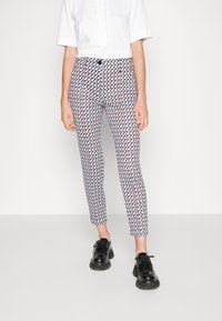 Pantalones con un diseño geométrico en rojo, azul y blanco; estilo ajustado con cierre de botón. Unos zapatos negros de cordones completan el conjunto.