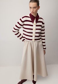 Pletený kardigan v krémové barvě s bordovými pruhy, s bordovým límcem a zlatými knoflíky. Doplněno o krémovou sukni a bordové boty.