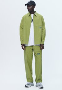 Green cotton shirt and pant set, featuring a button-up design, chest pocket, casual logo accent, paired with a white tee and gray sneakers.