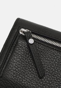 Borsa in pelle nera con superficie testurizzata, hardware della cerniera in argento e un'etichetta con il marchio sul cursore della cerniera.