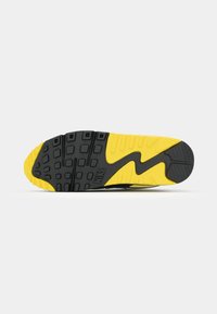 Black and yellow sneaker sole featuring textured patterns, logo, and a dynamic design, positioned on a plain white background.