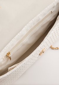 Cream woven clutch bag with gold clasp and zipper pocket inside, featuring chain strap partially visible on a white surface.