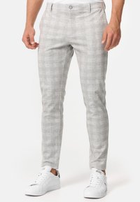 Gray checkered trousers made of smooth fabric with a tailored fit. Features a button closure and narrow legs. Paired with white sneakers.