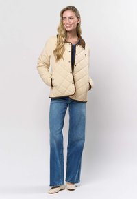 Beežist kroogitud jakk pruuni rõhuasetusega, millel on klõpsnööbid ja küljetaskud, kantud mereväesinise topi peale ning kombineeritud laiade sääreosadega teksapükstega.