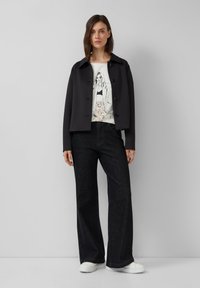 Veste noire courte avec des boutons, t-shirt graphique blanc, pantalon en denim foncé taille haute et baskets blanches. Finition douce, coupe décontractée.