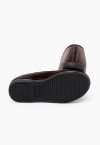 Scarpe in tessuto marrone con punta arrotondata, tacco basso e suola in gomma caratterizzata da linee di grip testurizzate; i lati sono lisci con dettaglio delle cuciture.