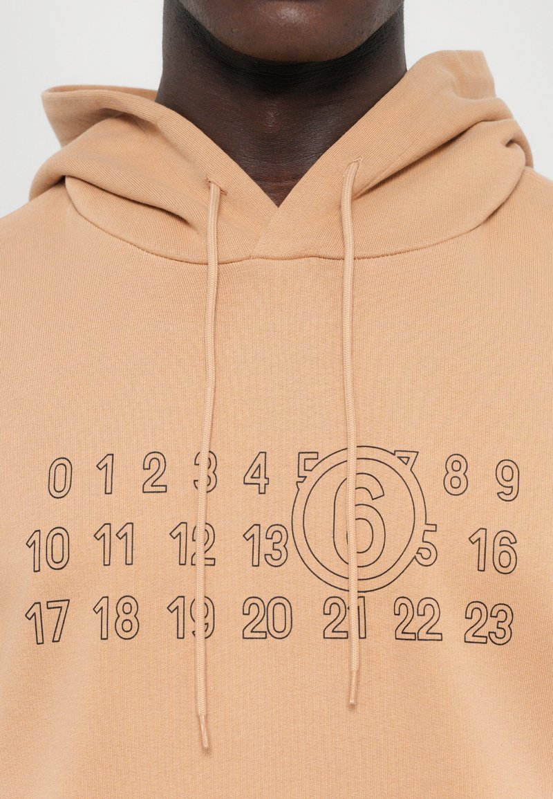 Kapuzensweatshirt aus hellbraunem Stoff mit einem grafischen Design, das Zahlen und einen Kreis um die "6" in Schwarz zeigt. Weicher Stoff.
