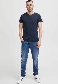 Marineblå kortærmet henley-skjorte med knapkrave, parret med lyseblå denimjeans og hvide sneakers med sorte striber.