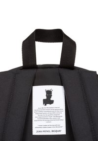 Bolso de tela negra con un exterior texturizado y asas cortas. En el interior, una etiqueta muestra una silueta y texto sobre el artista Jean-Michel Basquiat.