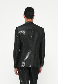 Zwarte sequined smokingjacket met een smalle revers, voorzien van een gestructureerd oppervlak en een slim fit, gedragen over bijpassende broeken.