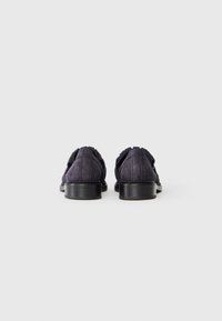 Des chaussures en suède violet foncé au design épuré, avec un bout arrondi et un tissu texturé. La semelle est noire et plate avec des coutures discrètes.