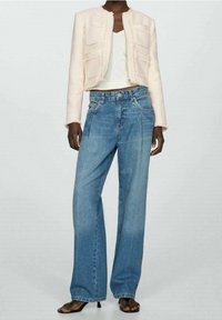 Lys pink cropped tekstureret jakke med to frontlommer, parret med lyseblå vide bukser. Outfittet inkluderer en hvid tanktop og sorte sandaler.