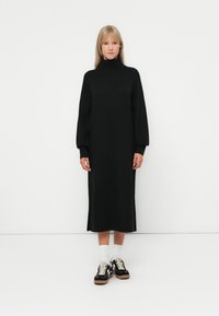 Melna adīta midi kleita ar augsto apkakli, garām pūkainām piedurkn�ēm un sānu šķēlumiem. Apvienota ar melniem sporta apaviem un baltām zeķēm. Gluda tekstūra.