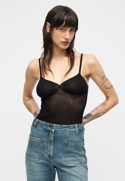 Μαύρο ριμπ κορμάκι με λεπτές τιράντες, λαιμόκοψη scoop και εφαρμοστή γραμμή, σε συνδυασμό με ανοιχτόχρωμο γαλάζιο τζιν ψηλόμεσο με ορατές τσέπες.