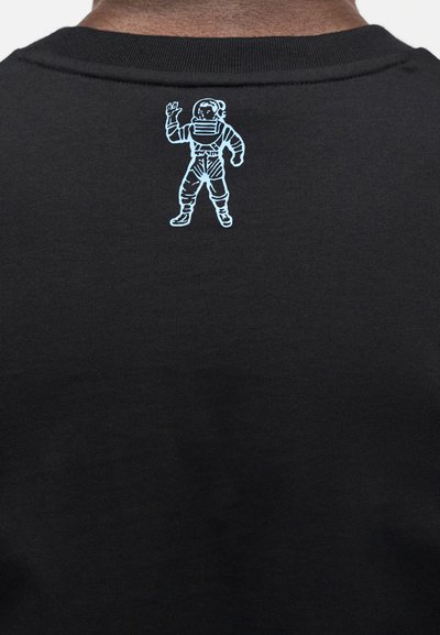 Μαύρο μπλουζάκι με υφή στην επιφάνεια· διαθέτει ένα ανοιχτό μπλε γραφικό αστροναύτη στην πλάτη, τοποθετημένο κοντά στη γραμμή του λαιμού.