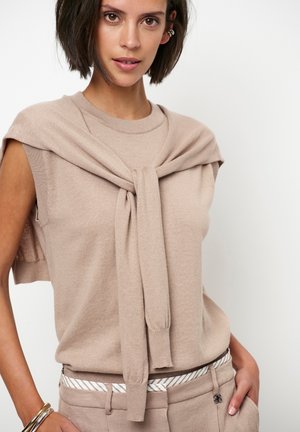 Beige trui met korte mouwen, gestrikt rond de nek, gemaakt van zachte stof. Gecombineerd met beige broek en een gestreepte riem.