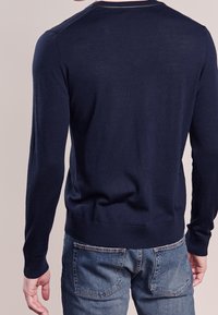 Marineblaues langärmeliges Sweatshirt aus leichtem Strickstoff, mit Rundhalsausschnitt und gerippten Bündchen und Saum. Getragen mit Jeans.
