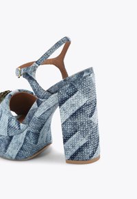 Sandalo con tacco in denim, caratterizzato da un design intrecciato in diverse tonalità di blu, cinturino alla caviglia regolabile e tacco grosso. Fodera interna marrone.