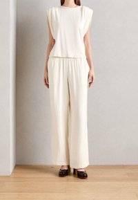 Crème-kleurig, losvallend top met korte pofmouwen en bijpassende wijde broek. Gladde textuur, casual ontwerp en platte zwarte schoenen.