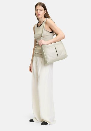 Bolso de hombro de cuero gris claro con dos bolsillos frontales, diseño elegante y correa ajustable. La modelo lleva pantalones de pierna ancha crema y una camiseta sin mangas beige.