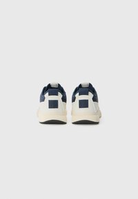Baskets de sport bleues et blanches avec un design élégant, un dessus texturé, un col rembourré et une semelle en caoutchouc contrastée. Détail du logo à l'arrière visible.