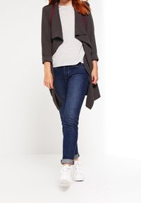 Grå öppen cardigan, grå t-shirt, mörkblå jeans och vita sneakers. Cardiganen har rullade ärmar och en flödande design.