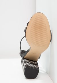 Svart lackläder högklackad sandal med en strukturerad plattform i silver och svarta ränder, med en slät, ribbad sula och smal ankelrem.