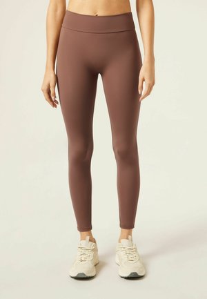 Brown athletic leggings with a high waist and smooth texture, paired with light-colored sneakers. The leggings offer a fitted silhouette.