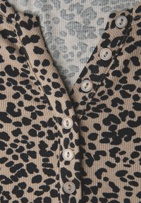 Beige gebreide stof met zwart luipaardprintpatroon en parelachtige knopen die verticaal zijn gerangschikt op een geribde V-halskleding.