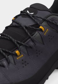 Κοντινό πλάνο σκούρου γκρίζου παπουτσιού πεζοπορίας με μαύρους και κίτρινους βρόχους κορδονιών και χοντρά, σχέδια μαύρα κορδόνια σε υφασμένο επάνω μέρος.