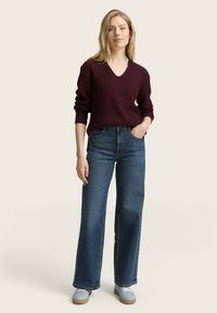 Pull en tricot côtelé bordeaux avec un col en V, associé à un jean bleu ample et des baskets bleu clair. Style simple et décontracté.