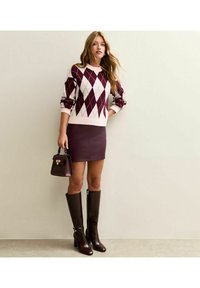 Maglione argyle bordeaux e crema, gonna in pelle bordeaux attillata, stivali marroni fino al ginocchio e una piccola borsa marrone con accenti metallici.