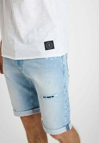 Lichtblauwe denimshorts met verwerkte accenten, opgerolde zomen en een logopatch op de achterzak. Zachte textuur en casual pasvorm.