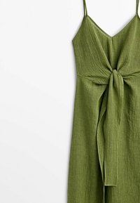 Robe verte sans manches avec fines bretelles et un détail lien en tissu à l'avant sur un matériau léger texturé.