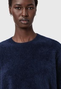Granatowy sweter wykonany z miękkiego, puszystego materiału z okrągłym dekoltem. Charakteryzuje się luźnym krojem i minimalnymi szwami, co daje gładki wygląd.