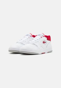 Valged sneakers punaste aktsentidega, nahast ülemine osa, pehmendatud krae ja kummist tallaosa, millel on tekstuuriga muster. Lacoste logo küljel.
