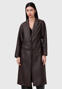 Cappotto in pelle marrone con un taglio lungo e dritto, rever a punta, due tasche anteriori e tre bottoni, caratterizzato da una texture liscia e un design minimalista.
