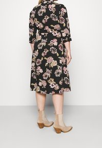 Black floral dress with three-quarter sleeves, belted waist, and beige ankle boots. Features pink and gold flower patterns against the dark background.