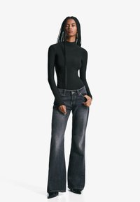 Svart långärmad bodysuit med hög halsringning, parat med mörka utsvängda jeans. Förslitna denim med standard femficksdesign och framknapp.